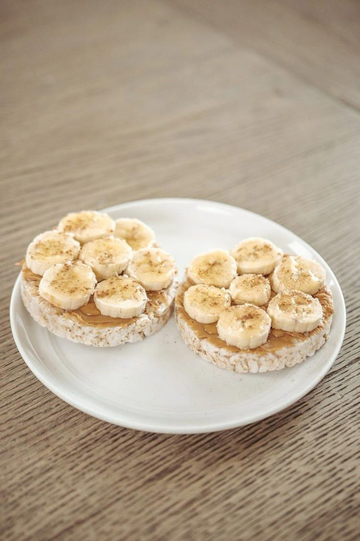 two pieces of bread with bananas on top are sitting on a white plate, ready to be eaten