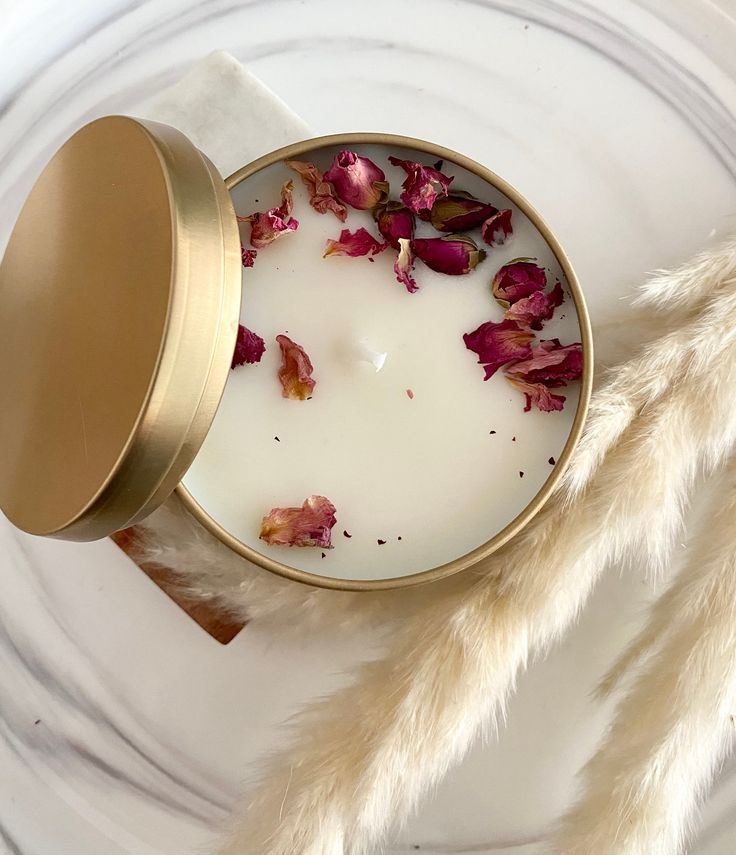 a white candle with rose petals in it on a marble surface next to a metal container