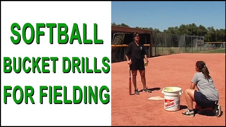 two girls are playing softball with buckets on the ground and one girl is holding a baseball bat