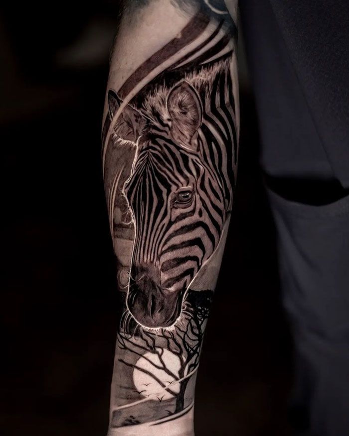 a man's arm with a zebra tattoo on it, and an animal in the background