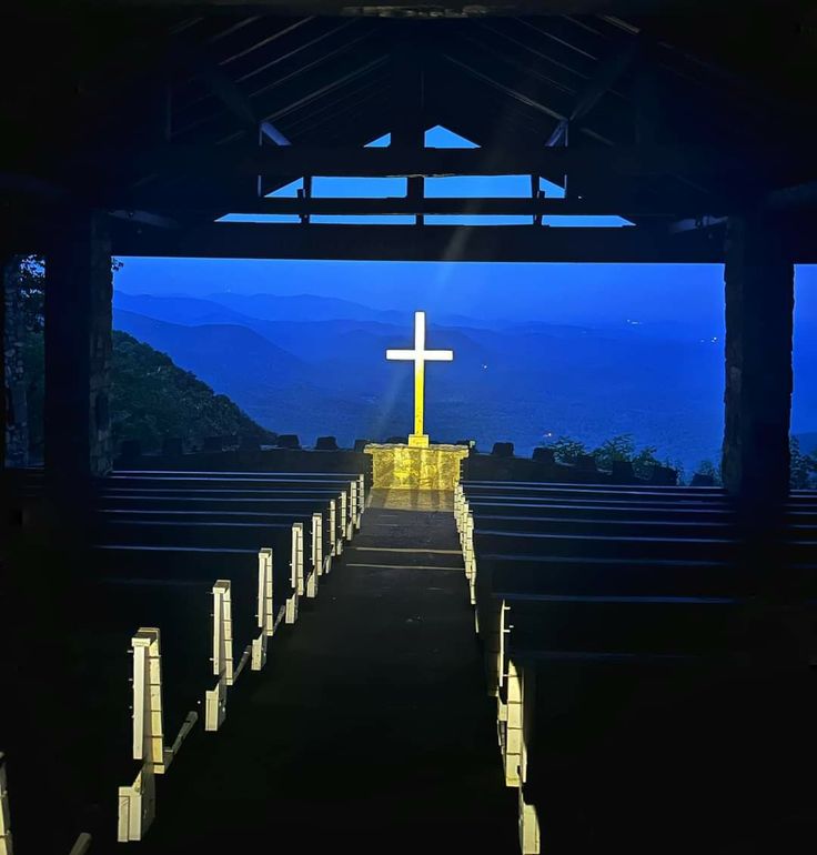 an empty church with a cross at the top and mountains in the distance behind it