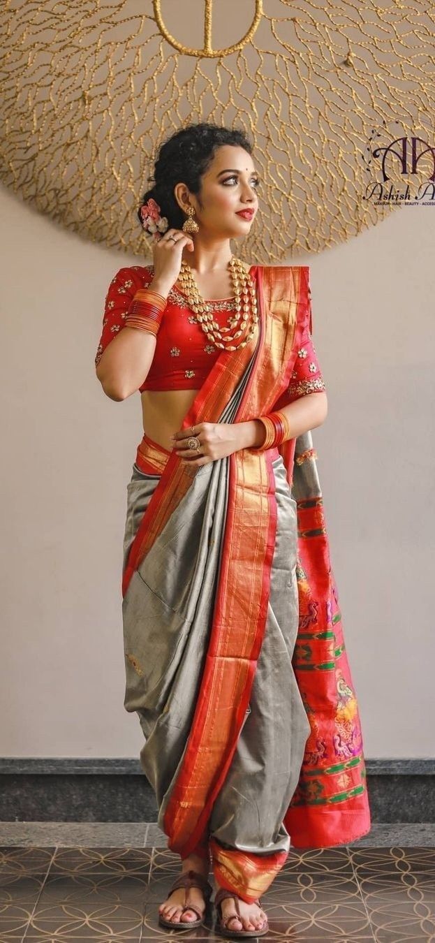 a woman in a red and grey sari is standing with her hand on her hip