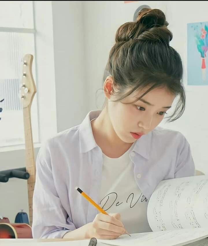 a woman sitting at a desk with a book and pencil in her hand while writing