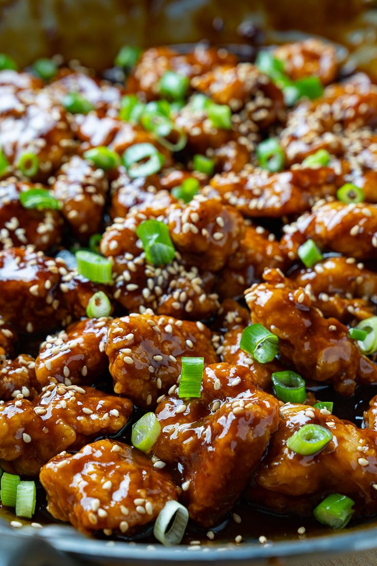 a pan filled with chicken covered in sesame seeds and green onions, topped with sesame seeds