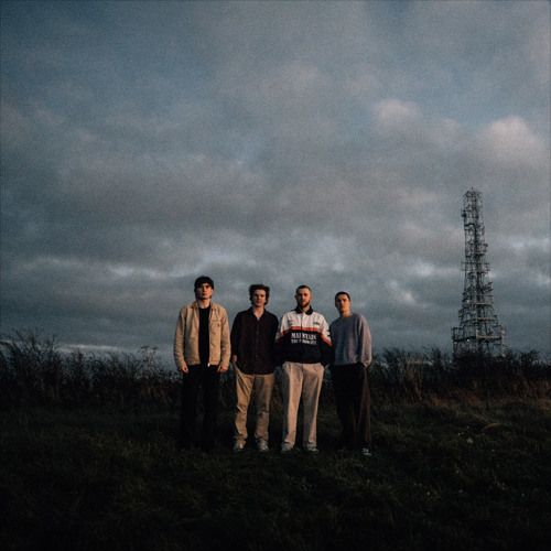 three men are standing in the grass with an antenna tower in the background on a cloudy day