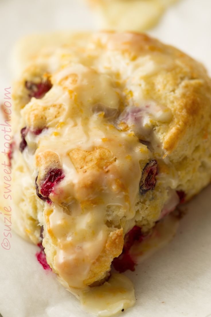 a close up of a muffin on a piece of paper with icing and cranberries