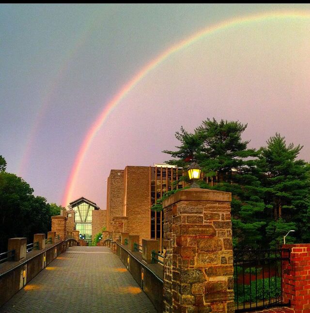 two rainbows are in the sky over a bridge with trees and brick walls on either side