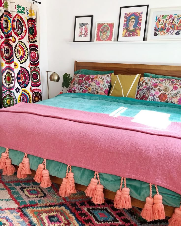 a bed with pink sheets and tassels in a room next to pictures on the wall