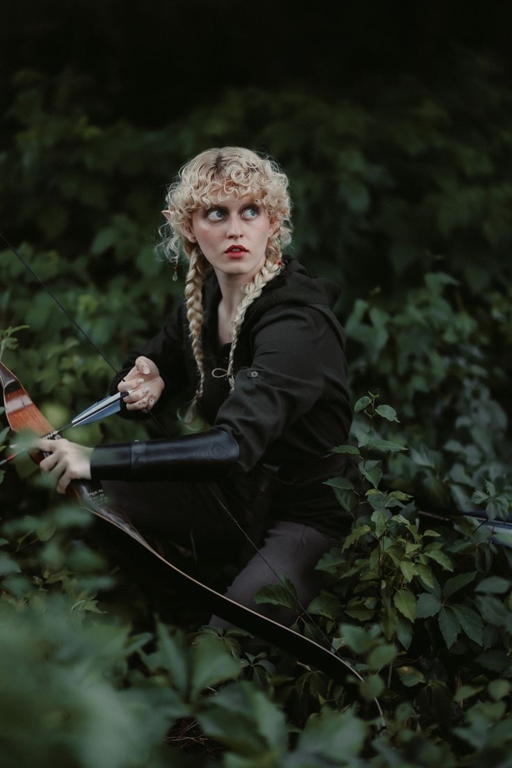 a woman with blond hair holding a bow and arrow in her hands while crouching on the ground