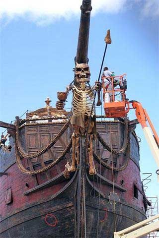 an old pirate ship is being worked on by crane operator and crew members, with skeleton hanging from the rigs