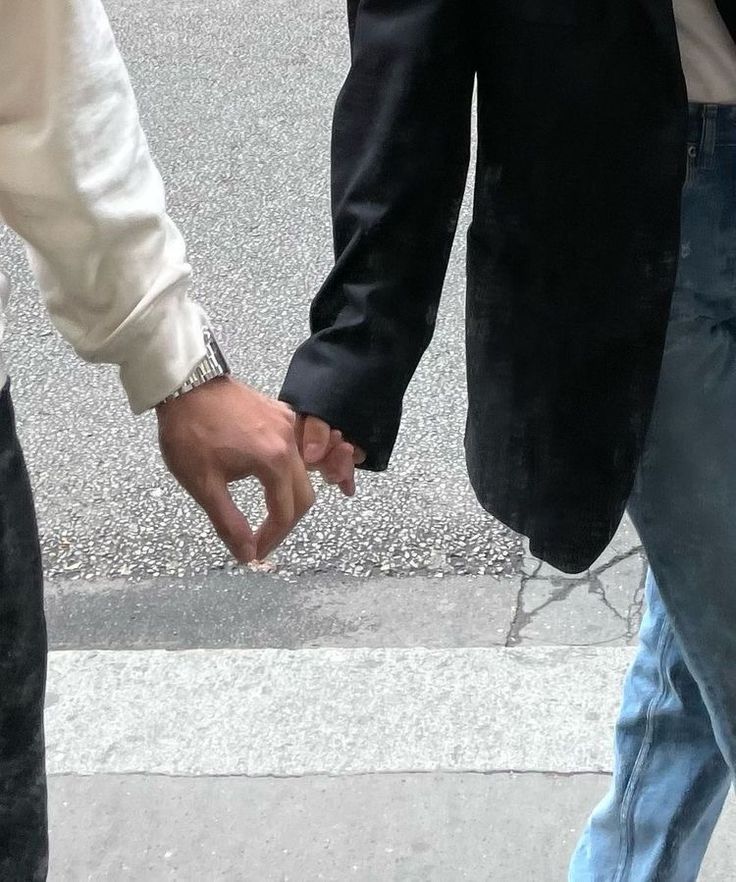 two people holding hands while walking down the street