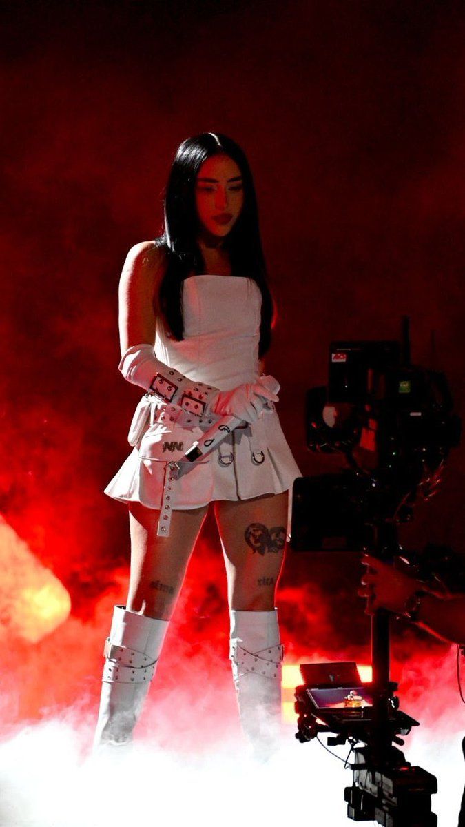 a woman in white dress and knee high boots standing next to a camera on stage