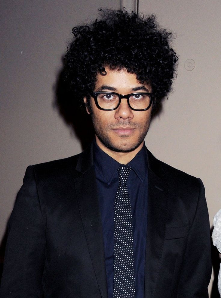 a man in a suit and tie with curly hair looking at the camera while wearing glasses