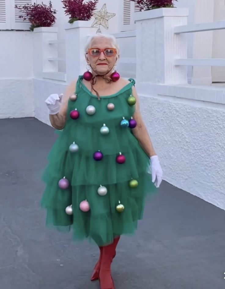 an older woman in a green dress with christmas ornaments on her neck and red boots