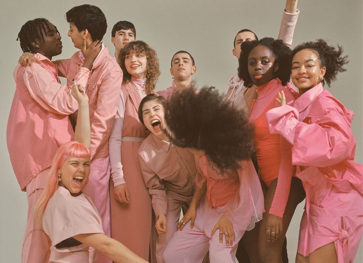 a group of people standing next to each other in front of a white wall with pink clothing on