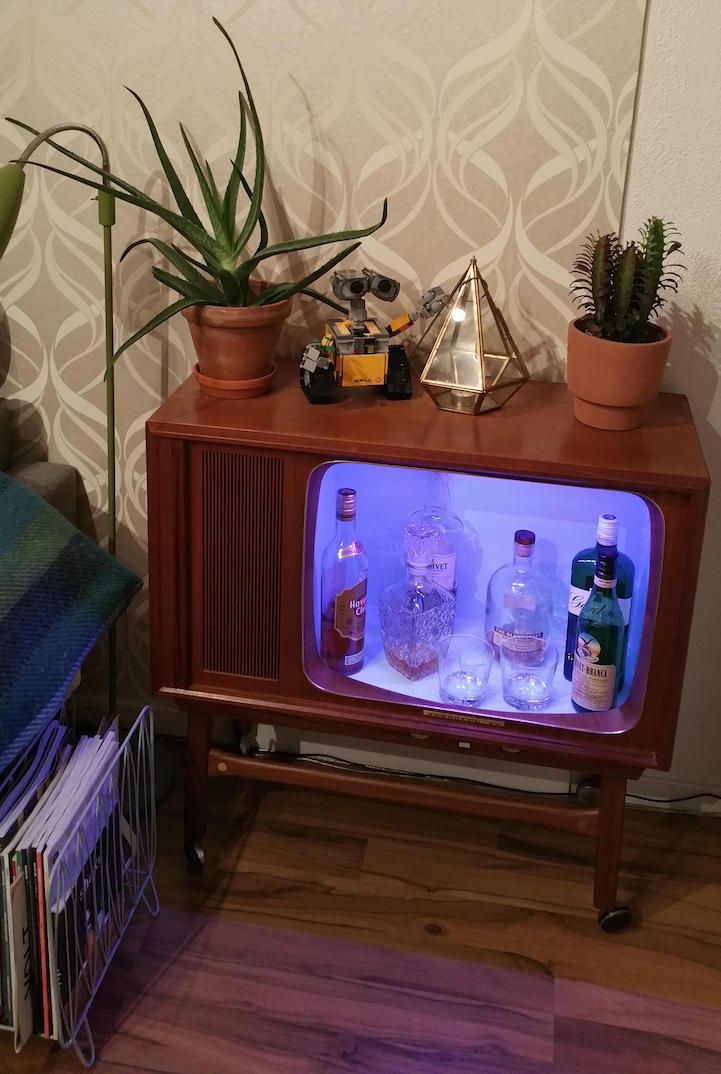 an old fashioned tv sitting on top of a wooden stand next to a potted plant