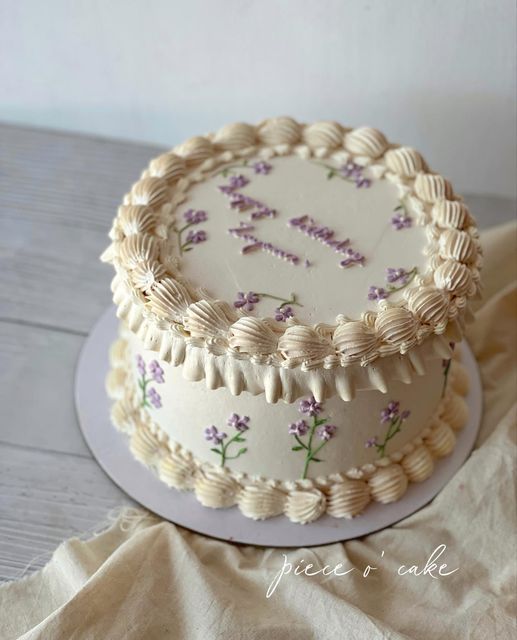 a decorated cake sitting on top of a wooden table next to a white plate with purple flowers