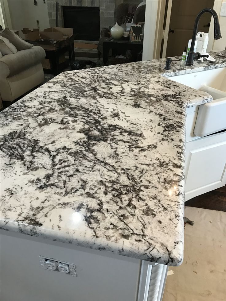 a kitchen counter top that is white and grey with black spots on the surface, in front of a living room