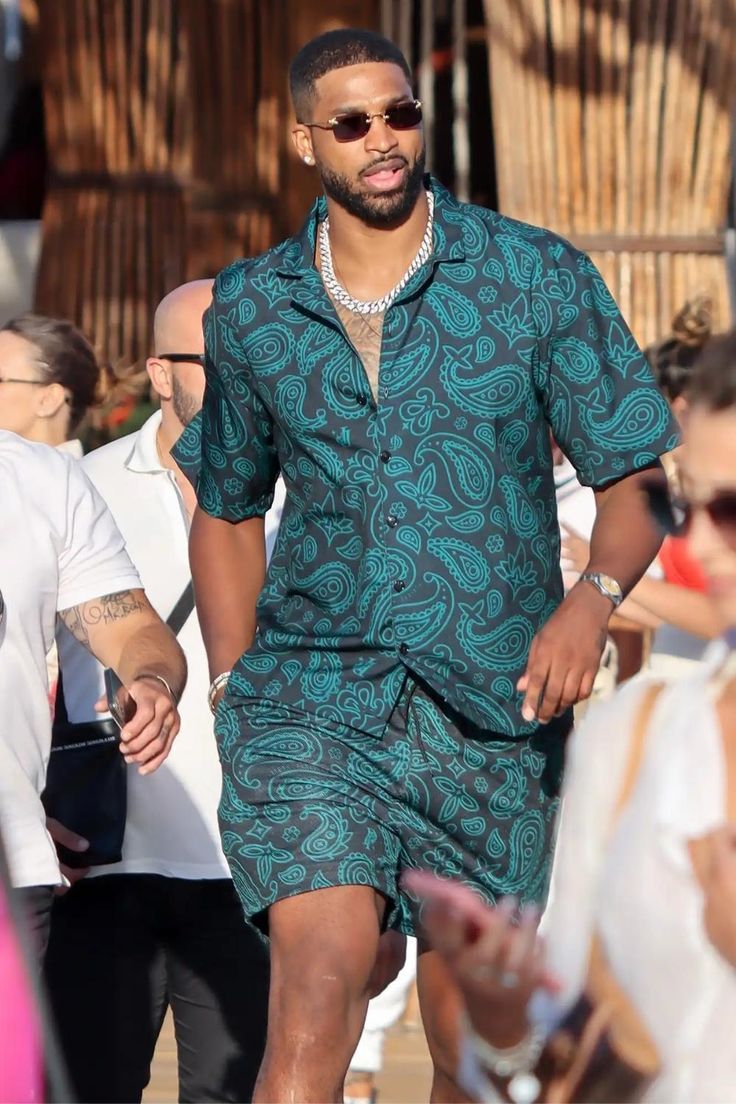 a man in a green shirt and shorts walking down the street with people behind him