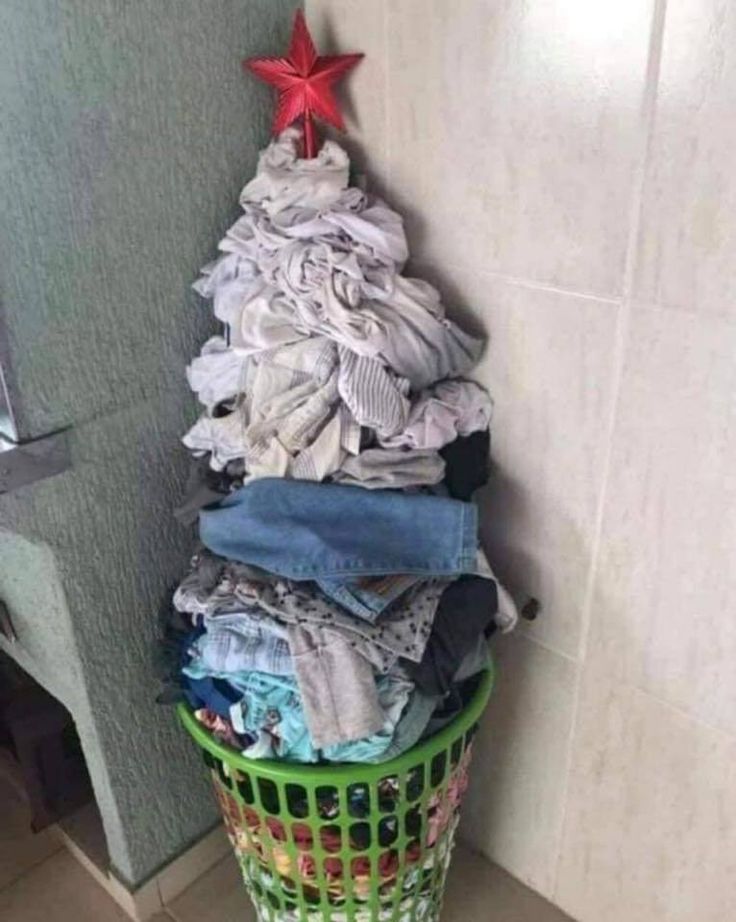 a pile of clothes sitting on top of a green trash can next to a wall