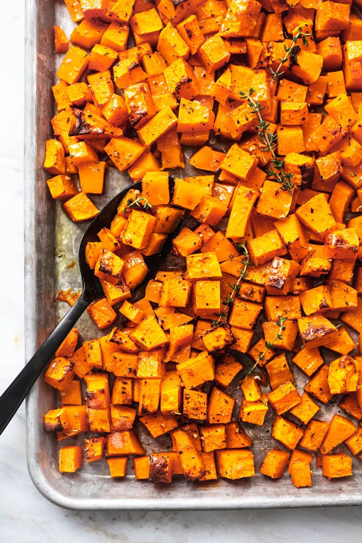 a pan filled with cooked sweet potatoes on top of a white countertop next to a black spoon