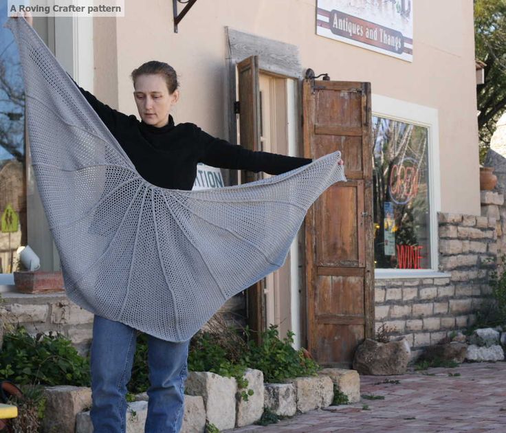 a woman holding up a shawl in front of a building