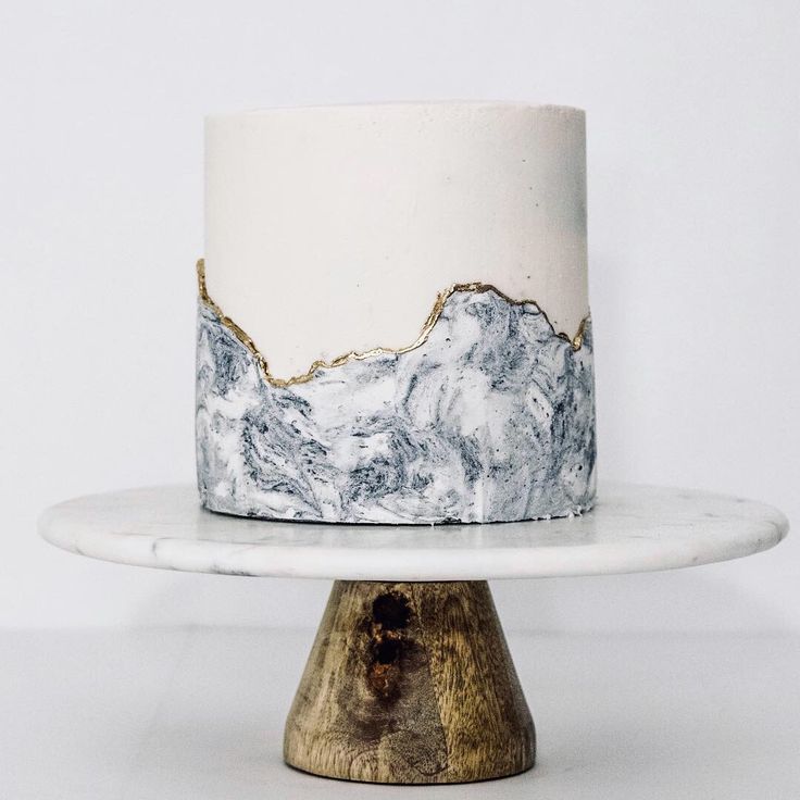 a marble cake with gold foiling on top and mountains in the background, sitting on a white pedestal