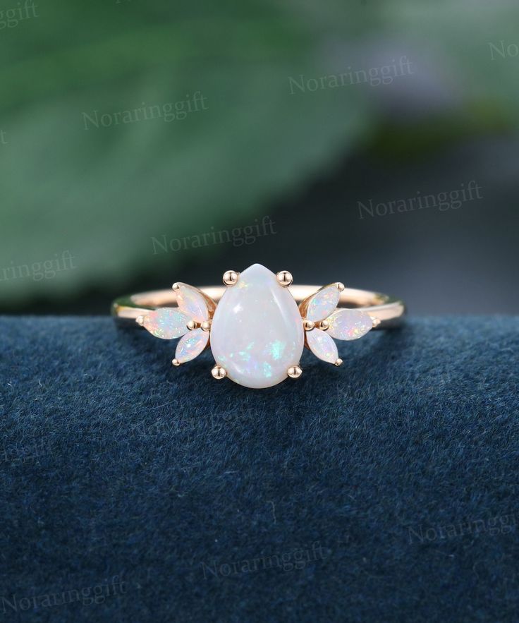 an opal and diamond ring sitting on top of a blue cloth