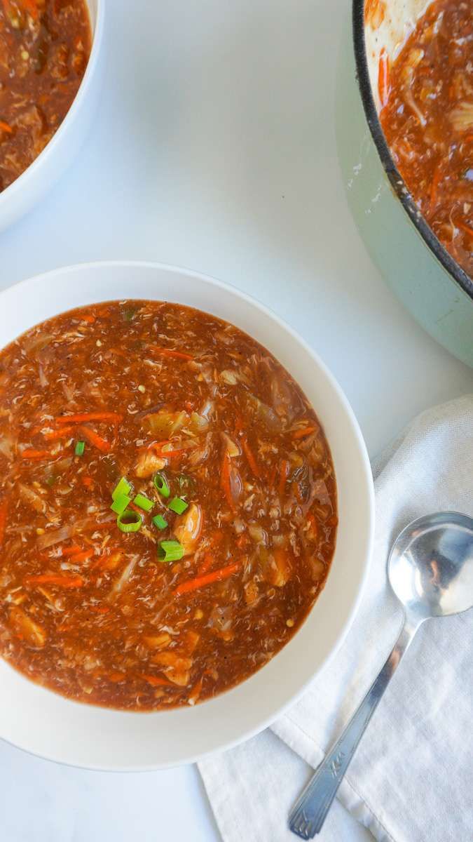 two bowls of soup on a white table with spoons and silverware next to it