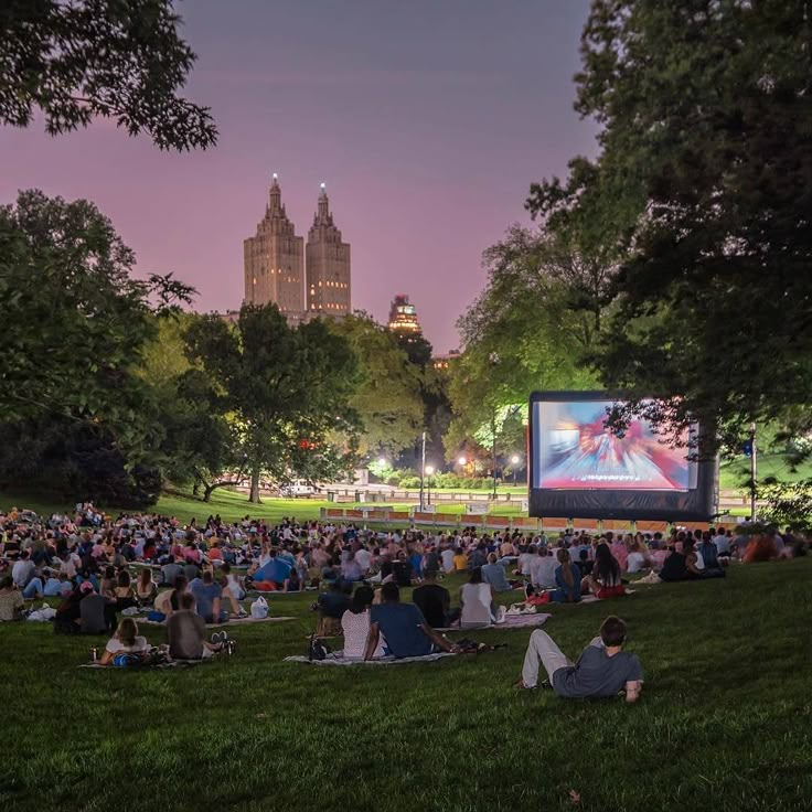 an outdoor movie in the park with people sitting on the grass watching it at night