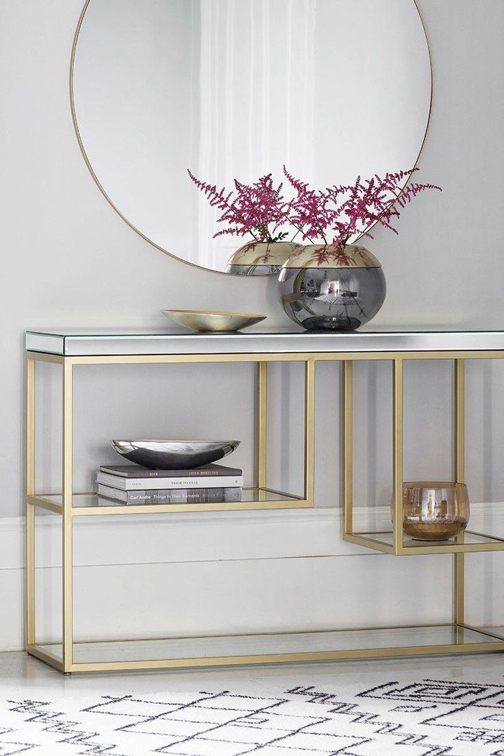 a console table with a mirror and vase on top, in front of a white wall