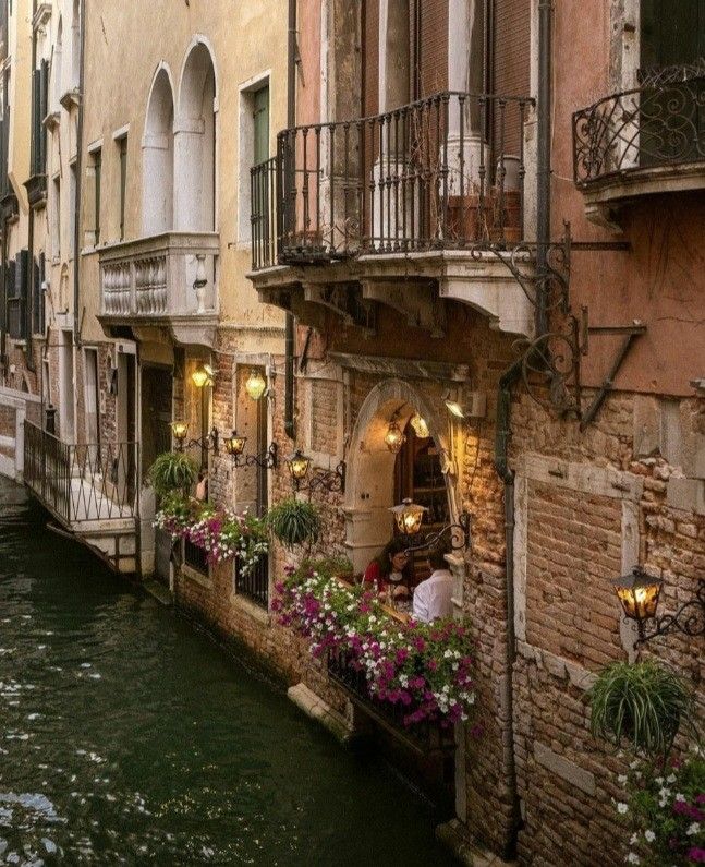 a narrow canal runs between two buildings with balconies and flowers in the windows