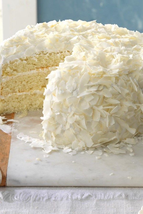 a white cake with coconut frosting on a cutting board next to a slice missing from it