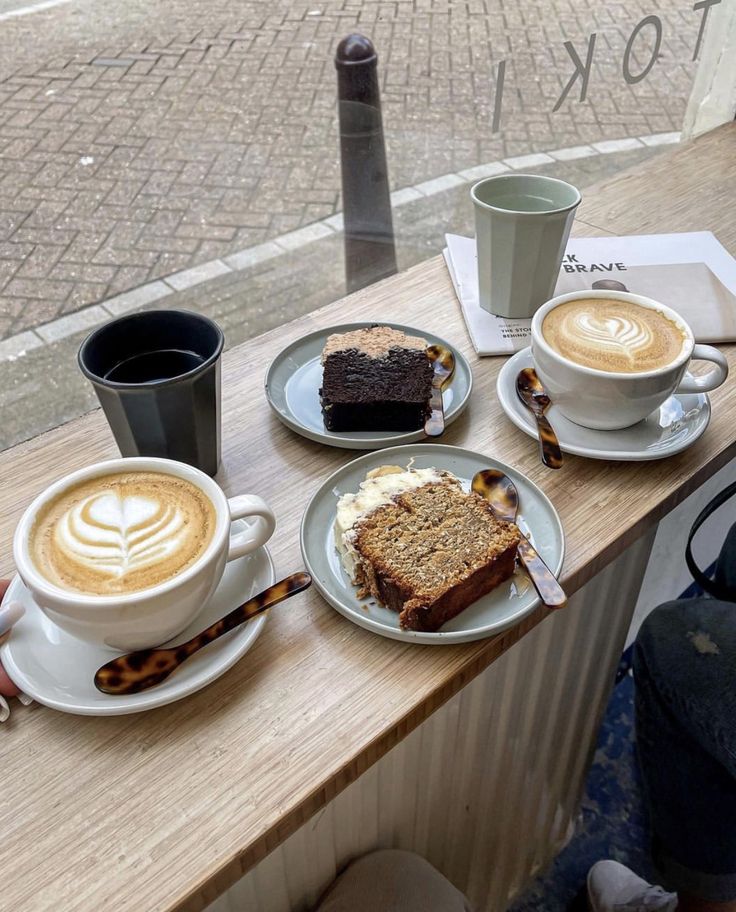 two plates with slices of cake on them next to cups of cappuccino