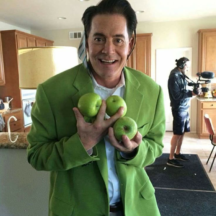 a man holding three green apples in his hands while standing next to a kitchen counter