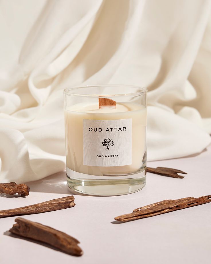 a glass candle sitting on top of a table next to some cinnamon sticks and cloves