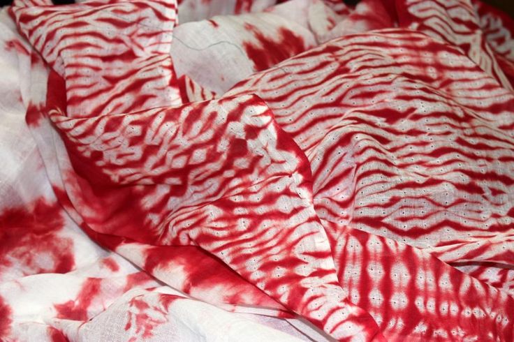 a red and white tie - dyed fabric is laying on top of a bed sheet