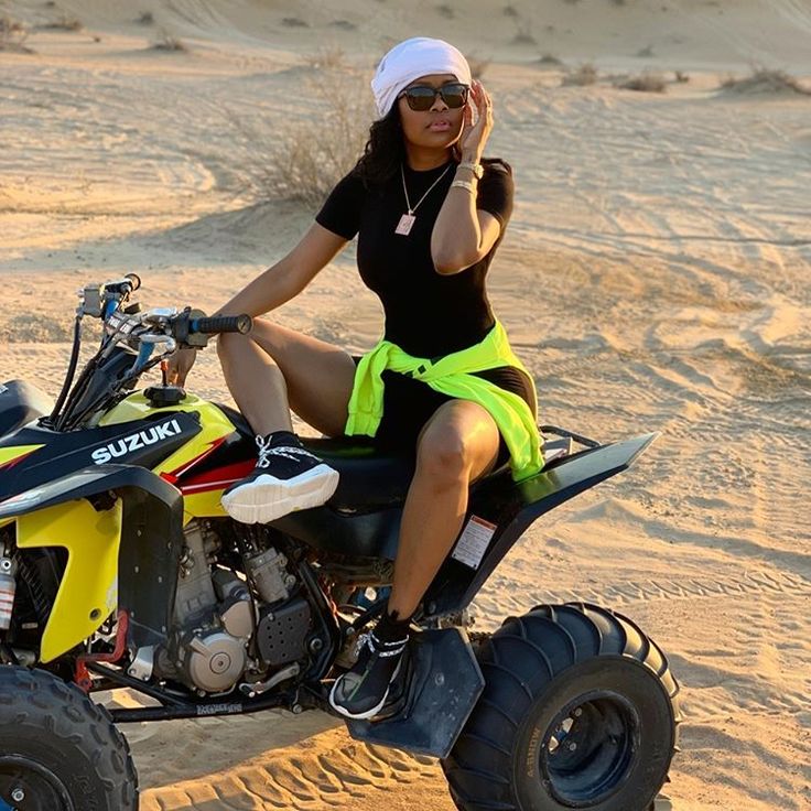 a woman sitting on top of a four wheeler in the desert while talking on her cell phone