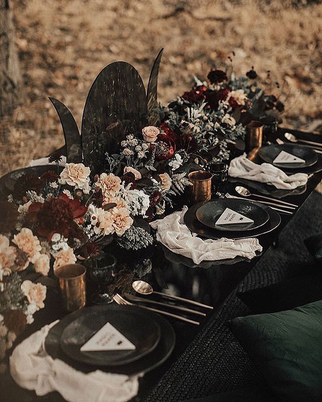 an outdoor table set up with black plates and floral centerpieces for dinner party