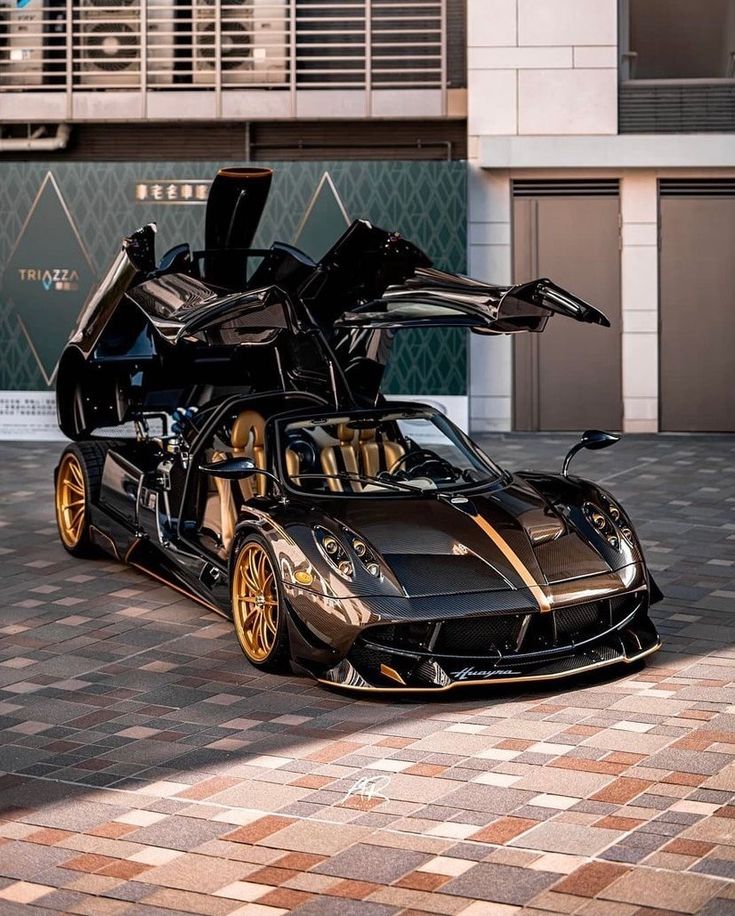 a black and gold sports car parked in front of a building with its doors open