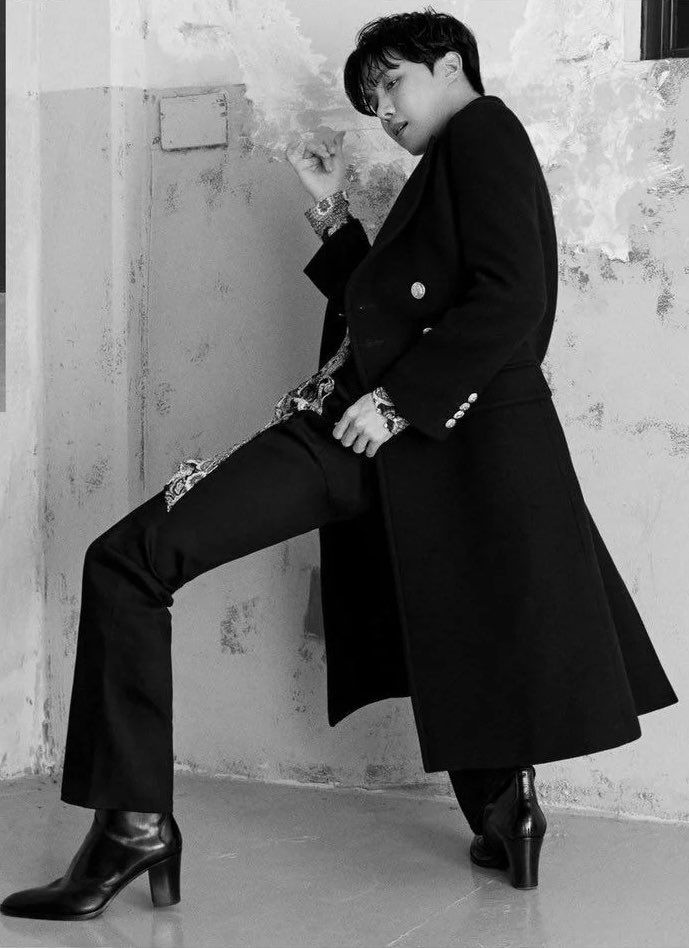 black and white photograph of a man in a coat leaning against a wall with his legs crossed