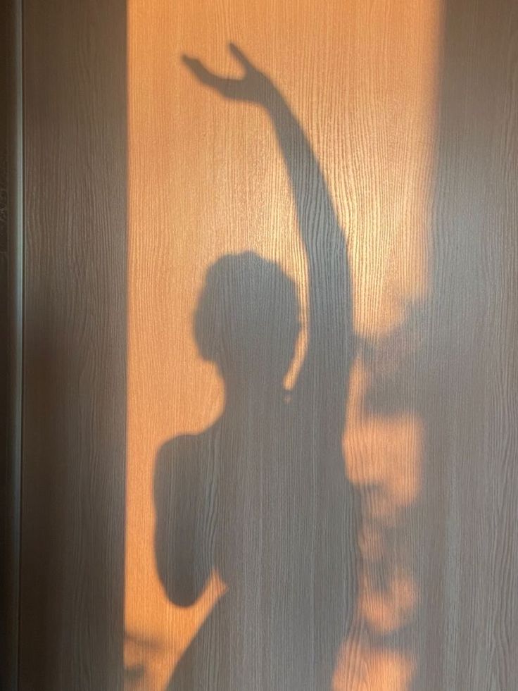 the shadow of a woman standing in front of a door with her hand up and arm extended