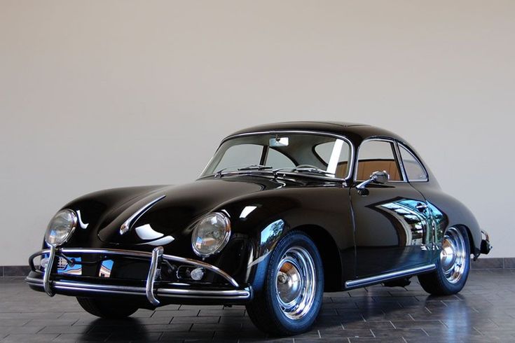 an old black car parked in a room with tile flooring and walls behind it