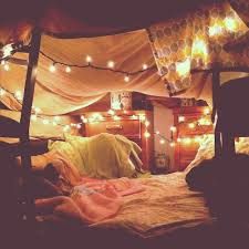 an unmade bed with lights strung from the ceiling and blankets on top of it