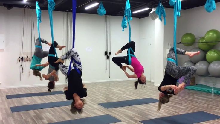 three women doing aerial acrobatic exercises in an exercise room with balloons and yoga mats