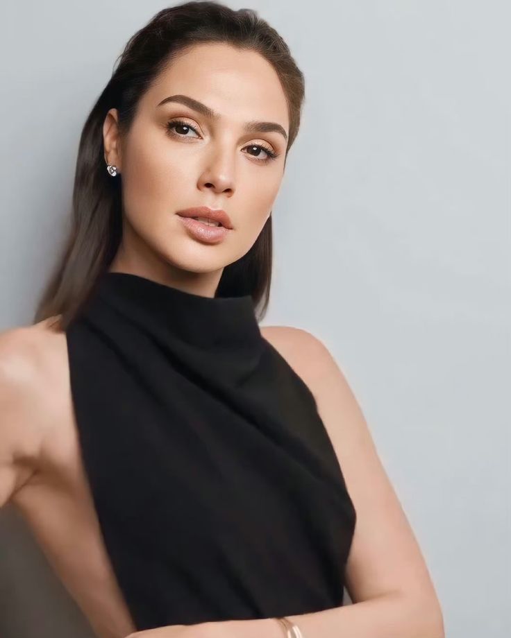 a woman in a black dress posing for the camera with her arms crossed and looking at the camera