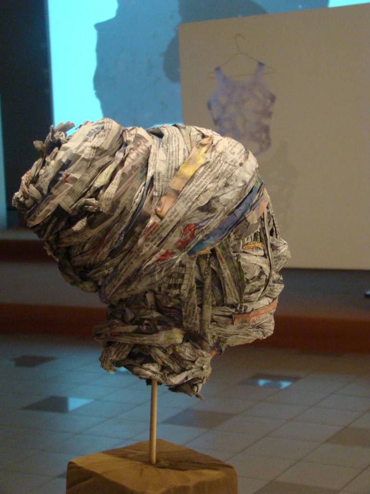 a sculpture made out of newspaper sitting on top of a wooden block in front of a wall