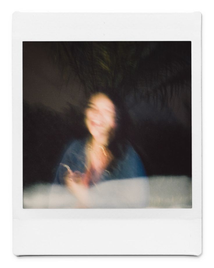 a blurry photo of a person sitting in front of a palm tree and holding a cell phone