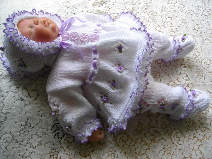 a baby doll laying on top of a white lace table cloth covered tablecloth with purple trim