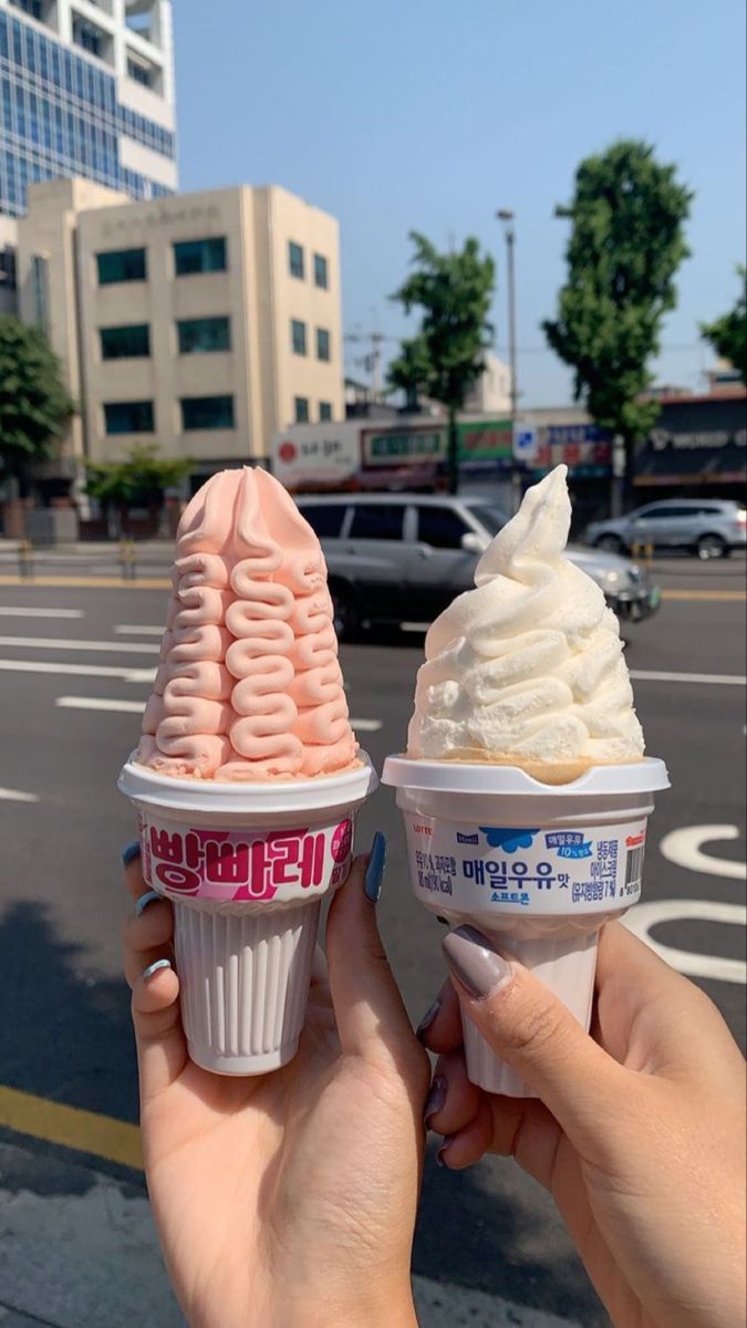 two ice cream cones with pink and white icing in front of a city street